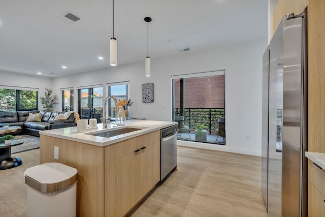 kitchen featuring light brown cabinetry, stainless steel appliances, a kitchen island with sink, sink, and pendant lighting