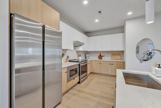 kitchen with tasteful backsplash, stainless steel appliances, sink, light hardwood / wood-style flooring, and white cabinetry