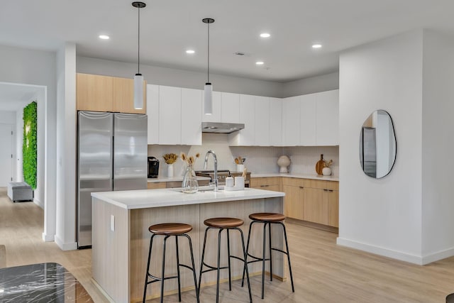 kitchen with stainless steel refrigerator, hanging light fixtures, light hardwood / wood-style floors, decorative backsplash, and a center island with sink