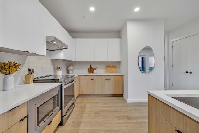 kitchen with ventilation hood, light wood-type flooring, white cabinetry, and appliances with stainless steel finishes