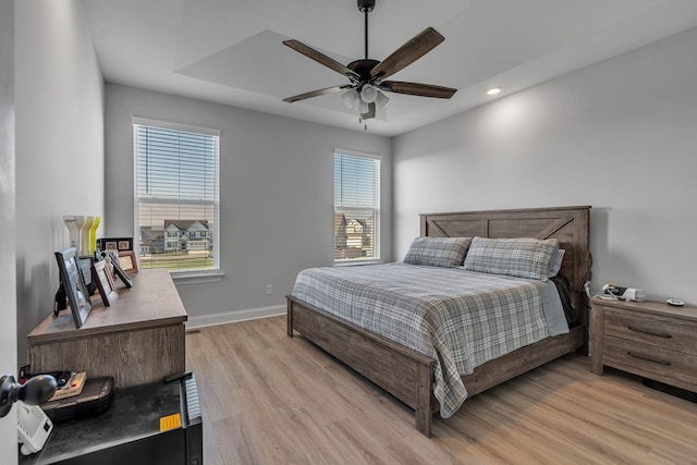 bedroom with a raised ceiling, ceiling fan, and light hardwood / wood-style flooring