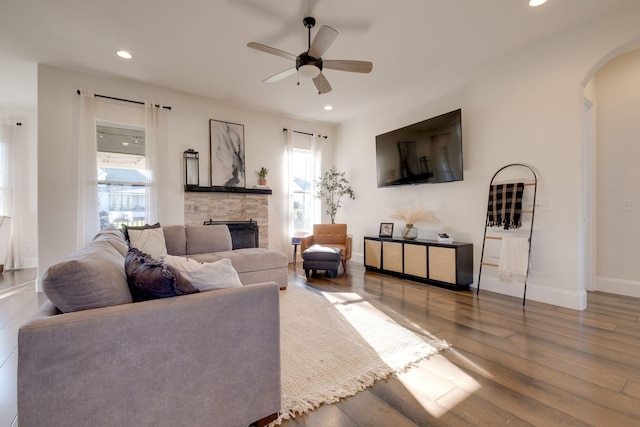 living room with a stone fireplace, ceiling fan, and wood-type flooring