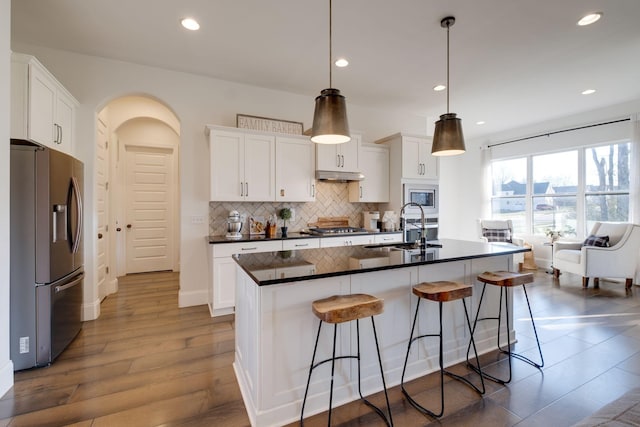 kitchen featuring white cabinetry, sink, stainless steel appliances, decorative light fixtures, and a kitchen island with sink