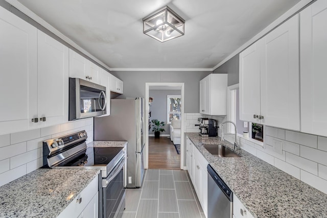 kitchen featuring appliances with stainless steel finishes, light stone counters, white cabinets, backsplash, and sink