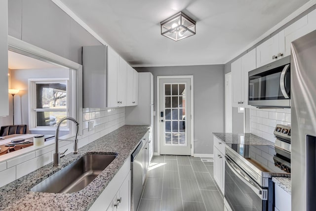 kitchen featuring stainless steel appliances, light stone countertops, white cabinets, backsplash, and sink