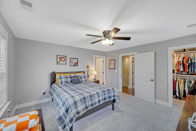 bedroom featuring ceiling fan, multiple windows, a walk in closet, light carpet, and a closet