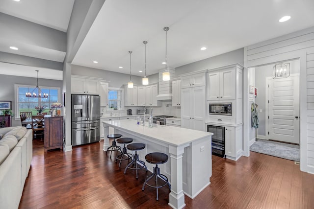 kitchen featuring decorative light fixtures, a breakfast bar area, a center island with sink, white cabinets, and appliances with stainless steel finishes