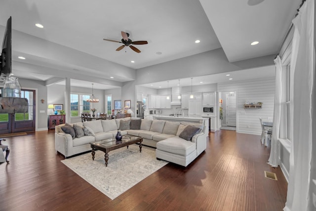 living room featuring ceiling fan with notable chandelier and dark wood-type flooring