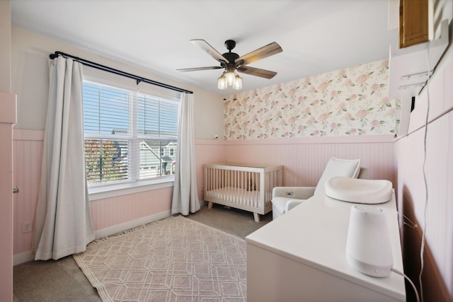 carpeted bedroom featuring ceiling fan and a nursery area