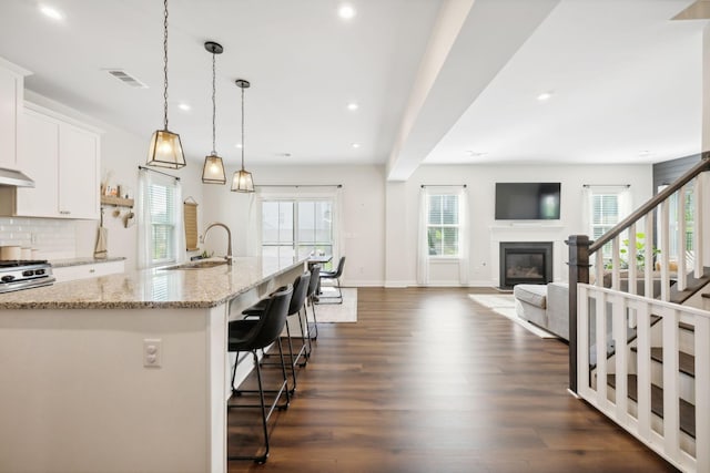 kitchen featuring pendant lighting, white cabinets, sink, an island with sink, and light stone counters