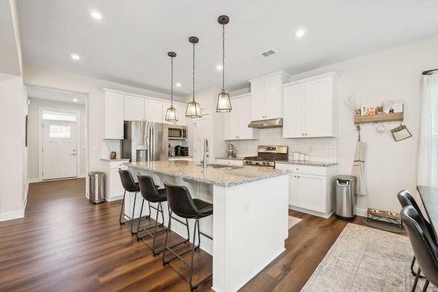 kitchen with hanging light fixtures, light stone counters, a kitchen island with sink, white cabinets, and appliances with stainless steel finishes