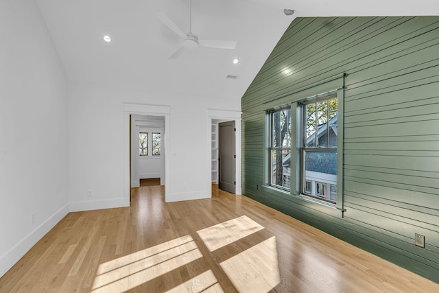 spare room with light wood-type flooring, high vaulted ceiling, ceiling fan, and wood walls