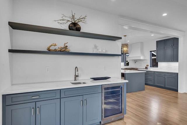 bar featuring sink, beverage cooler, light stone counters, decorative light fixtures, and custom range hood