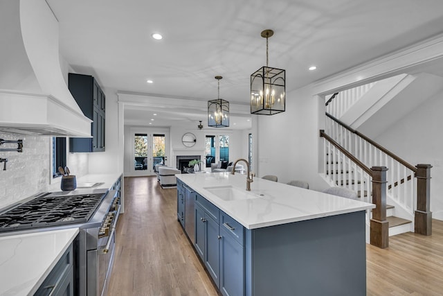 kitchen with sink, light hardwood / wood-style floors, pendant lighting, a center island with sink, and custom exhaust hood