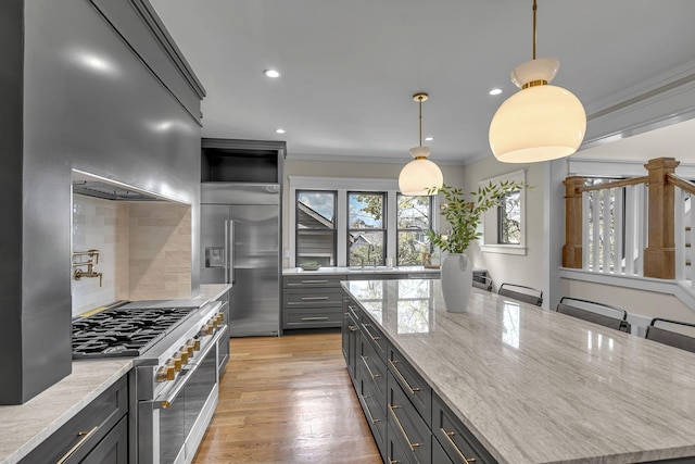 kitchen with pendant lighting, decorative backsplash, ornamental molding, premium appliances, and light stone counters