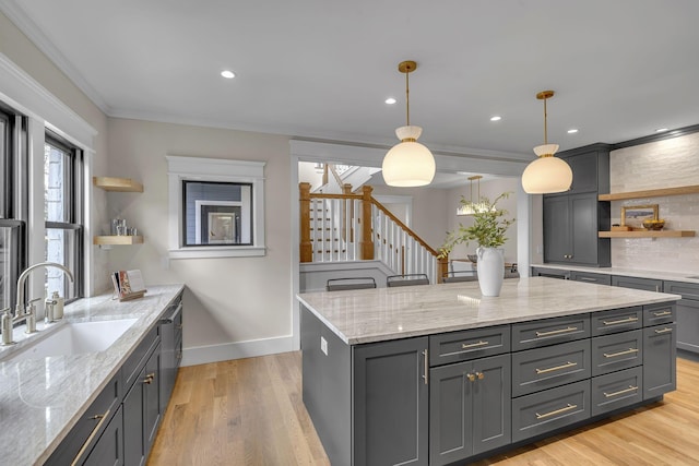 kitchen featuring light stone countertops, sink, light hardwood / wood-style floors, decorative light fixtures, and ornamental molding