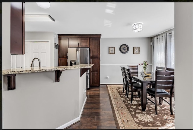 kitchen with stainless steel fridge, a breakfast bar, dark brown cabinets, light stone countertops, and dark hardwood / wood-style flooring