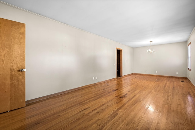 spare room with hardwood / wood-style flooring and an inviting chandelier