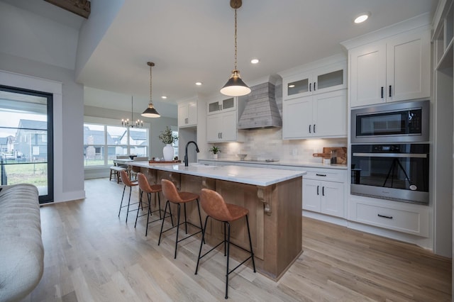 kitchen with wall chimney exhaust hood, built in microwave, decorative light fixtures, white cabinets, and oven