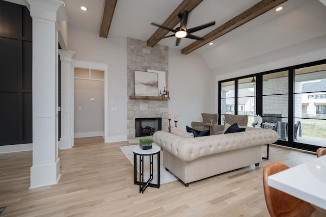 living room with lofted ceiling with beams, light hardwood / wood-style flooring, ceiling fan, and a stone fireplace