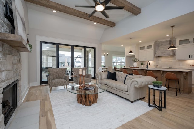 living room with vaulted ceiling with beams, ceiling fan with notable chandelier, light wood-type flooring, and a fireplace