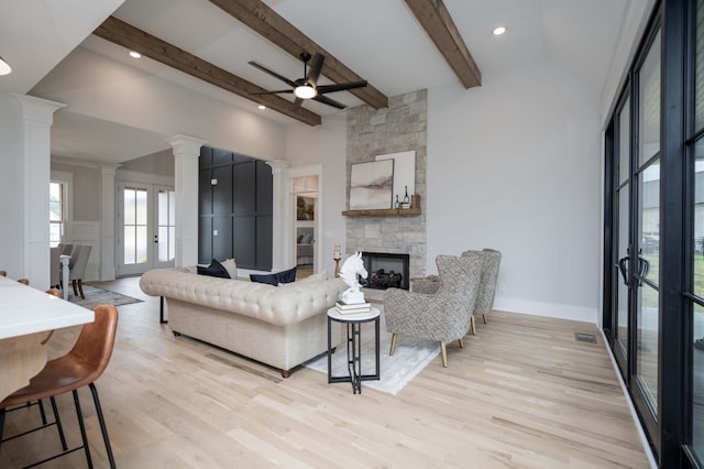 living room featuring beam ceiling, ceiling fan, decorative columns, light hardwood / wood-style floors, and a fireplace