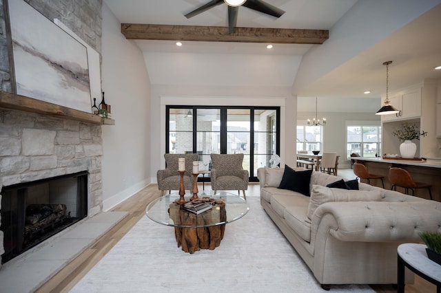 living room with a stone fireplace, light hardwood / wood-style flooring, ceiling fan with notable chandelier, and vaulted ceiling with beams