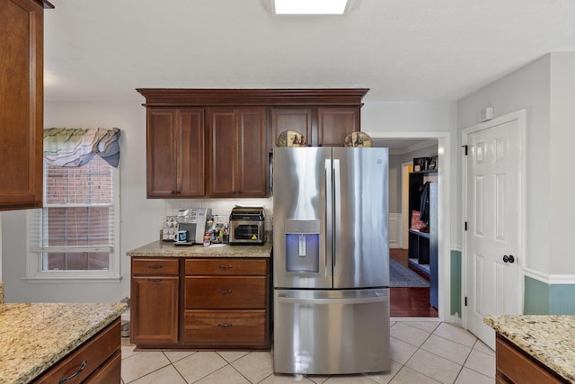 kitchen featuring stainless steel fridge, light stone counters, light tile patterned floors, and backsplash