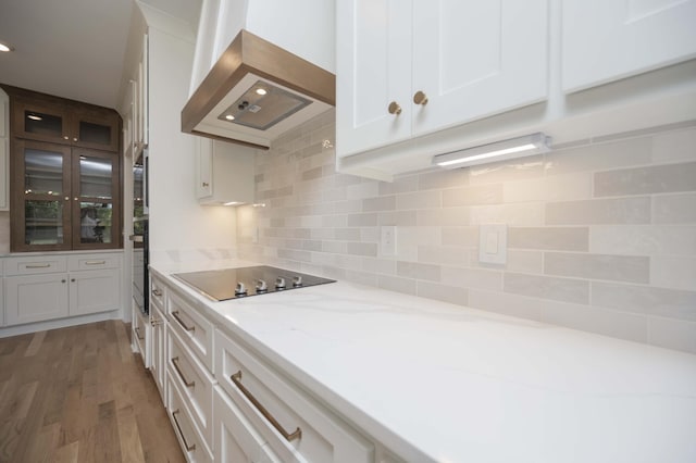 kitchen with backsplash, black appliances, white cabinets, range hood, and light stone counters