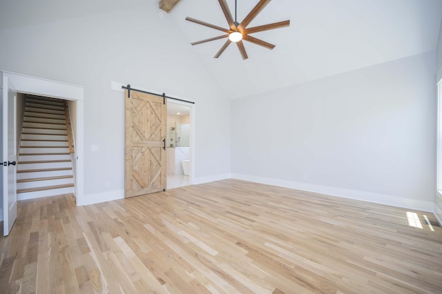 empty room featuring beam ceiling, ceiling fan, a barn door, high vaulted ceiling, and light hardwood / wood-style floors