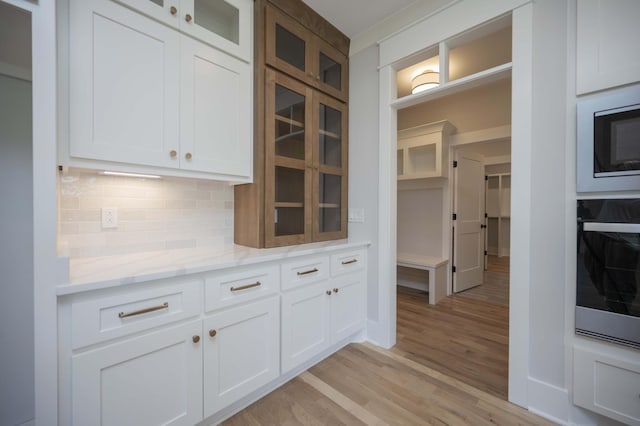 kitchen featuring light wood-type flooring, tasteful backsplash, light stone counters, white cabinets, and oven