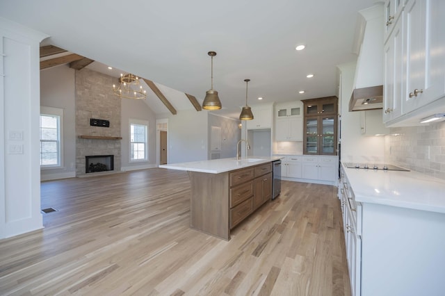 kitchen with a kitchen island with sink, stainless steel dishwasher, a fireplace, tasteful backsplash, and white cabinetry