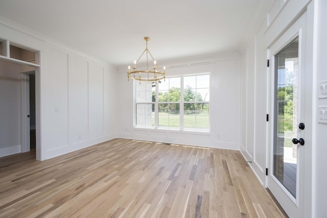 unfurnished dining area with light wood-type flooring, an inviting chandelier, and ornamental molding