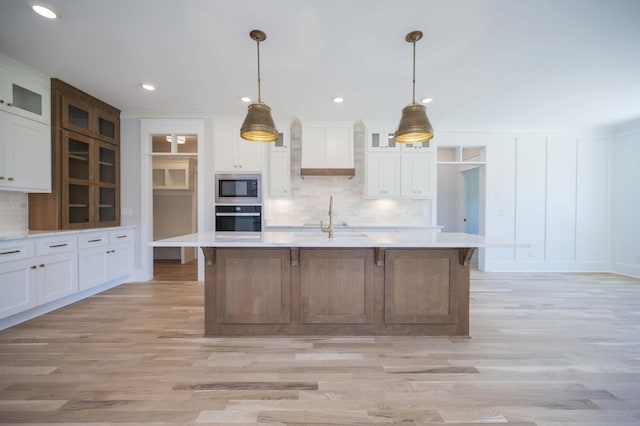 kitchen featuring a large island with sink, built in microwave, stainless steel oven, and white cabinets