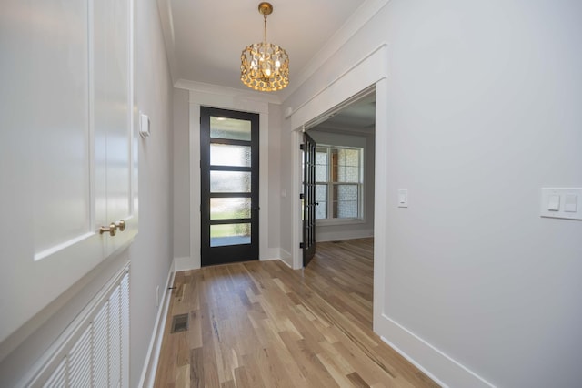 entryway featuring light wood-type flooring, crown molding, and an inviting chandelier