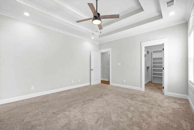 unfurnished bedroom featuring a raised ceiling, a walk in closet, crown molding, ceiling fan, and a closet