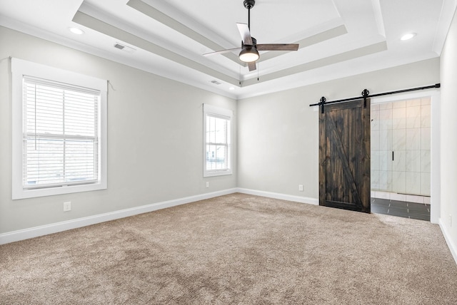 empty room with carpet floors, a barn door, a tray ceiling, and ornamental molding