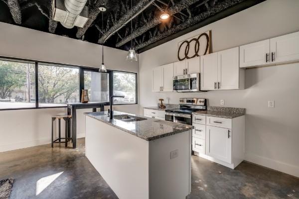 kitchen featuring a kitchen island with sink, white cabinets, sink, dark stone countertops, and stainless steel appliances