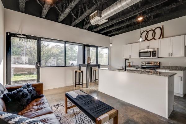 kitchen featuring hanging light fixtures, stainless steel appliances, an island with sink, dark stone counters, and white cabinets