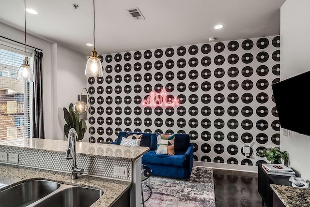 kitchen with decorative light fixtures, light stone counters, and sink