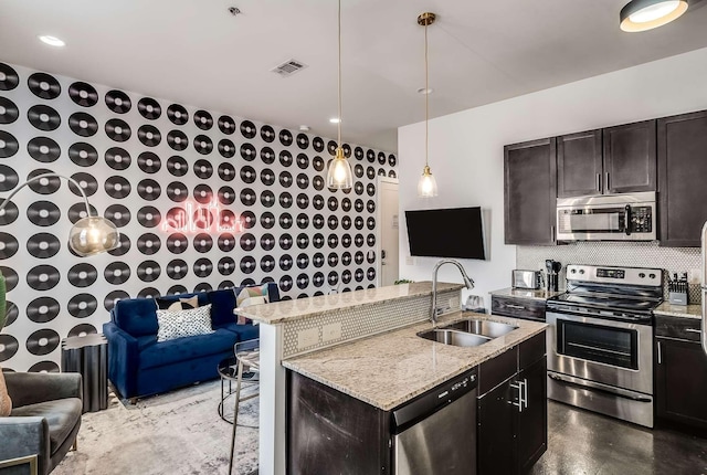 kitchen with hanging light fixtures, sink, light stone countertops, appliances with stainless steel finishes, and dark brown cabinetry