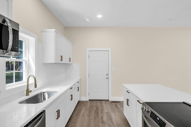 kitchen with sink, stainless steel appliances, backsplash, white cabinets, and light wood-type flooring