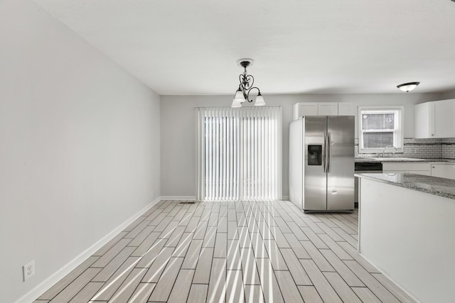 kitchen featuring hanging light fixtures, an inviting chandelier, tasteful backsplash, stainless steel refrigerator with ice dispenser, and white cabinets