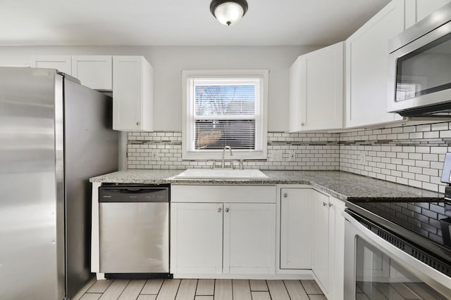 kitchen with light stone countertops, white cabinetry, sink, and appliances with stainless steel finishes