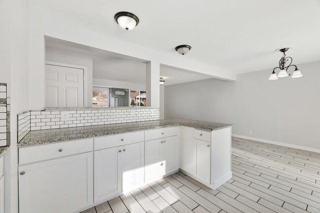 kitchen with kitchen peninsula, decorative backsplash, light hardwood / wood-style flooring, white cabinetry, and hanging light fixtures