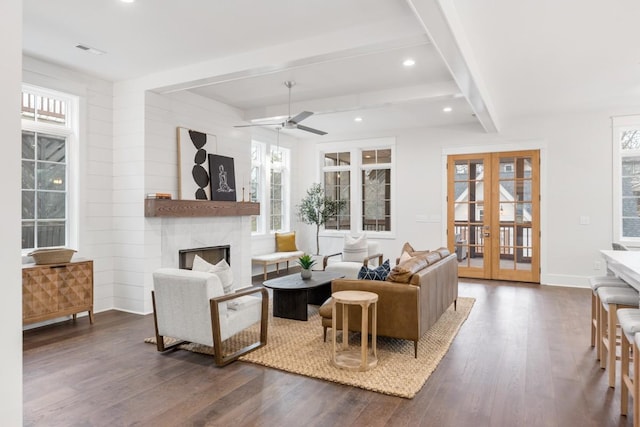 living room featuring french doors, a large fireplace, ceiling fan, beam ceiling, and dark hardwood / wood-style floors