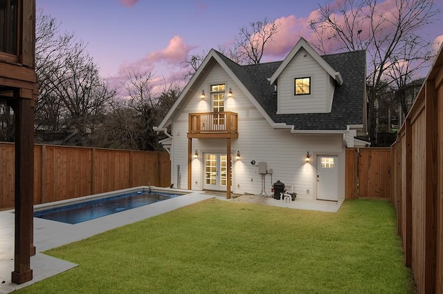 back house at dusk featuring a balcony, a fenced in pool, a yard, and a patio