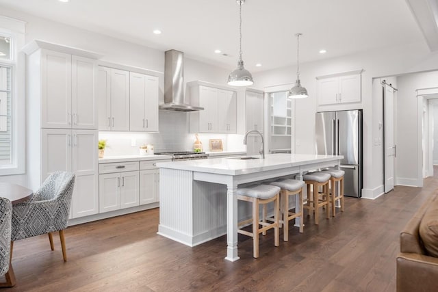 kitchen with stainless steel refrigerator, sink, wall chimney range hood, a center island with sink, and white cabinets