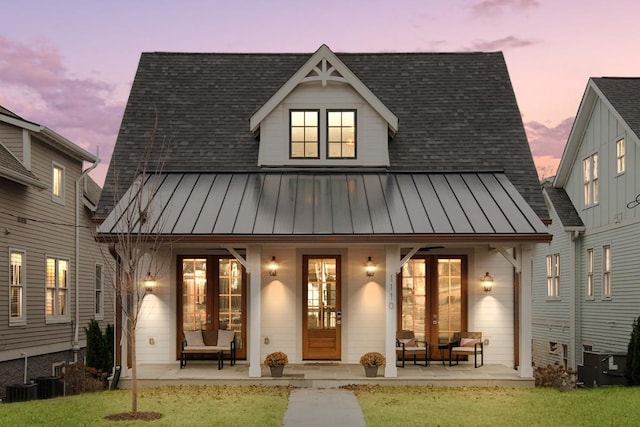 back house at dusk featuring a yard, covered porch, and central AC unit