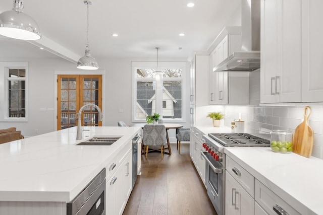 kitchen featuring a center island with sink, white cabinets, wall chimney range hood, and stainless steel appliances